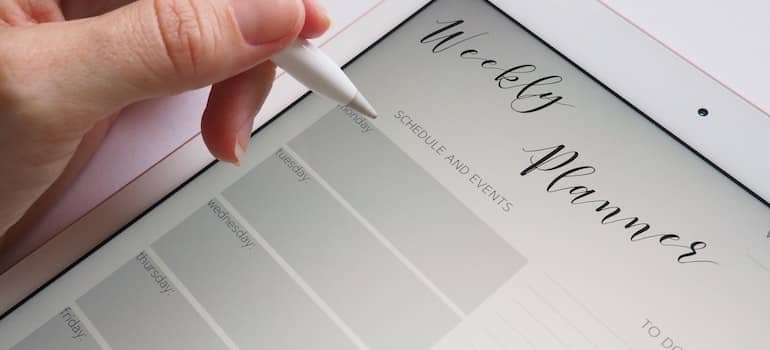 A woman holding an Ipad with a weekly planner app opened;